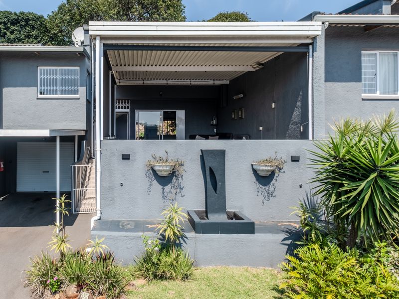 Front elevation of a townhouse featuring a covered patio, integrated water feature, and an attached garage with a roller door.