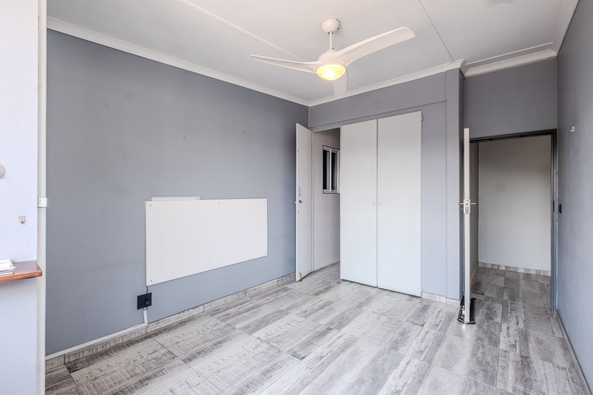 An empty bedroom featuring grey walls, light-toned laminate flooring, a ceiling fan, and built-in storage cupboards.