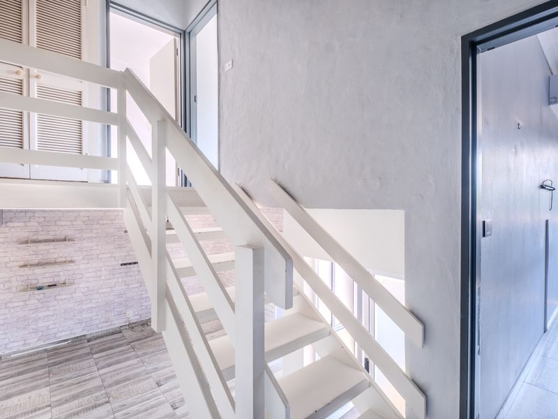 A bright, empty hallway featuring a white staircase, built-in storage cupboards, and tiled flooring, providing access to multiple areas of the townhouse.