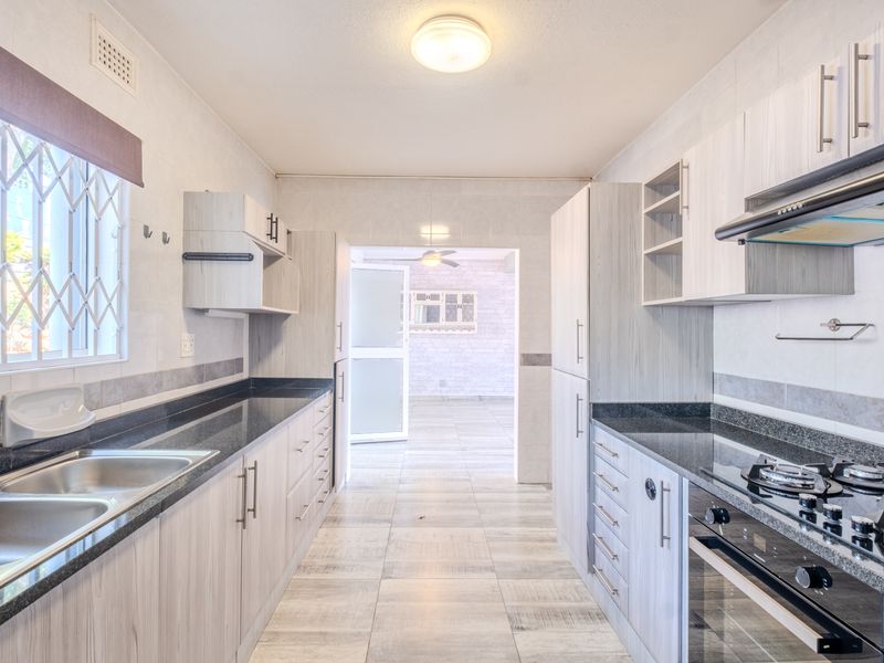 A clean and functional galley-style kitchen featuring modern light wood cabinetry, granite countertops, a gas hob, and an integrated oven.