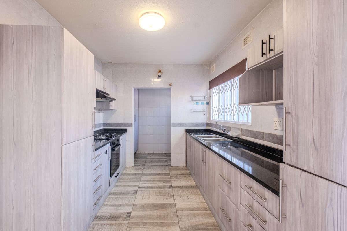 A clean, functional kitchen featuring light wood-grain cabinetry, dark granite countertops, built-in oven, gas hob, and tiled flooring with a separate scullery area.