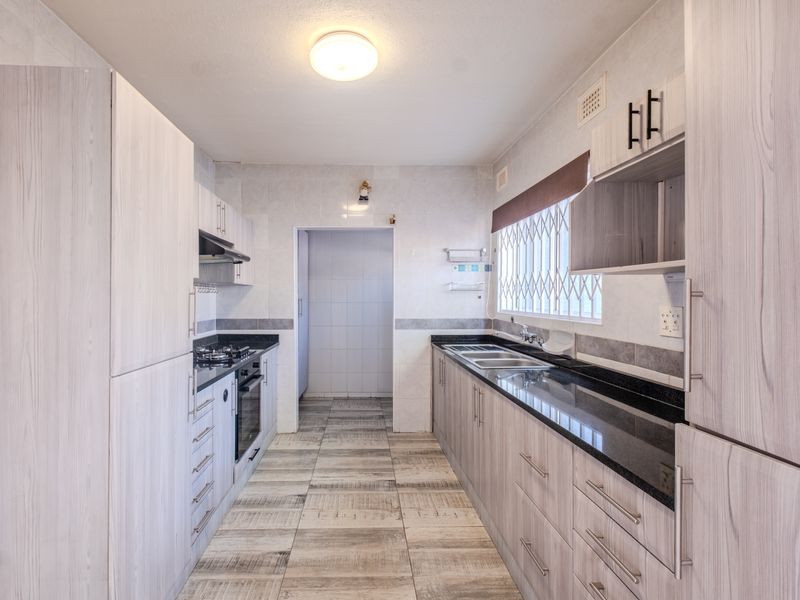 A clean, functional kitchen featuring light wood-grain cabinetry, dark granite countertops, built-in oven, gas hob, and tiled flooring with a separate scullery area.