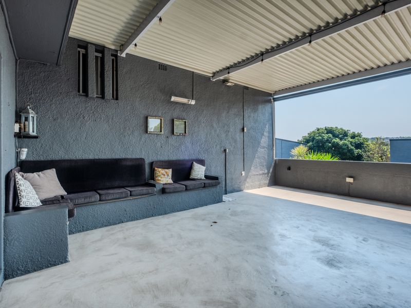 Spacious covered patio featuring a built-in concrete bench, textured dark walls, and a corrugated metal roof, offering a functional outdoor entertainment space.