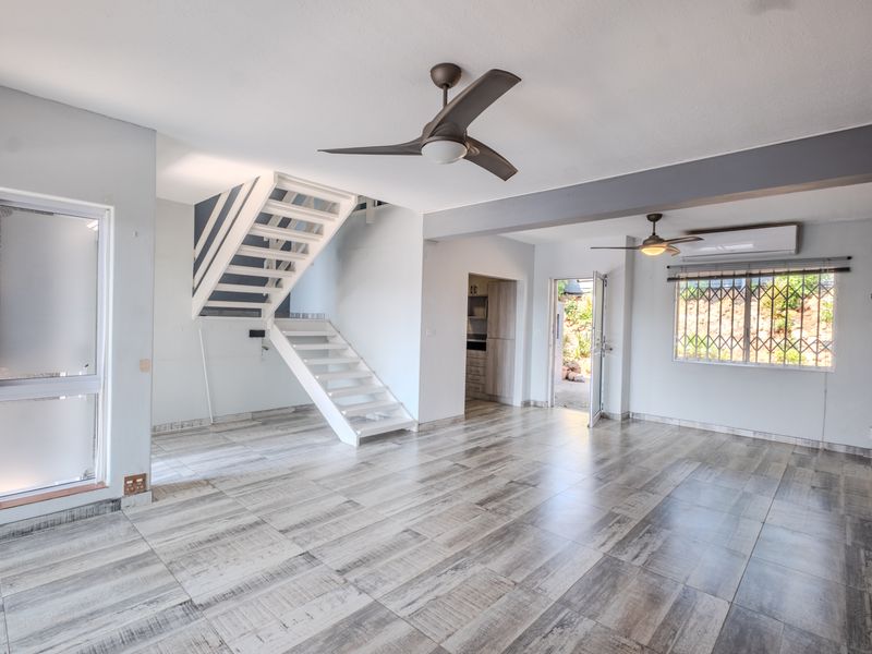 Spacious open-plan living area featuring modern tiled flooring, a central staircase, ceiling fans, and air conditioning, offering a bright and versatile layout.