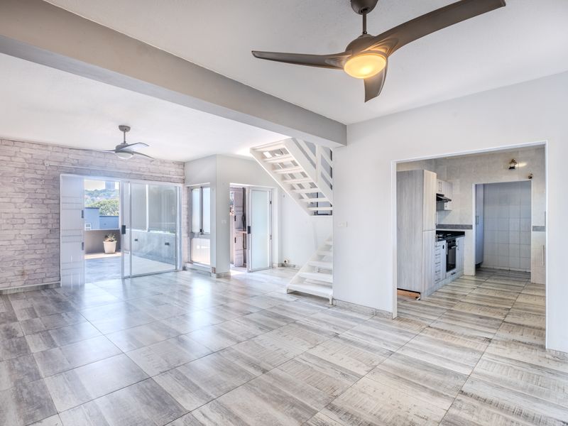 Spacious open-plan living area featuring modern tiled floors, a feature brick wall, ceiling fans, and a staircase leading to the upper level.