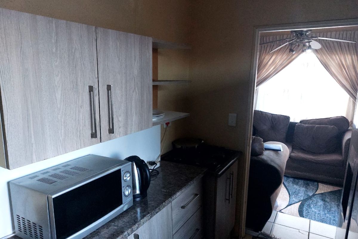 Compact kitchen featuring modern laminate cabinetry, stone-look countertops, and a built-in stove, with direct access to the adjacent living area.