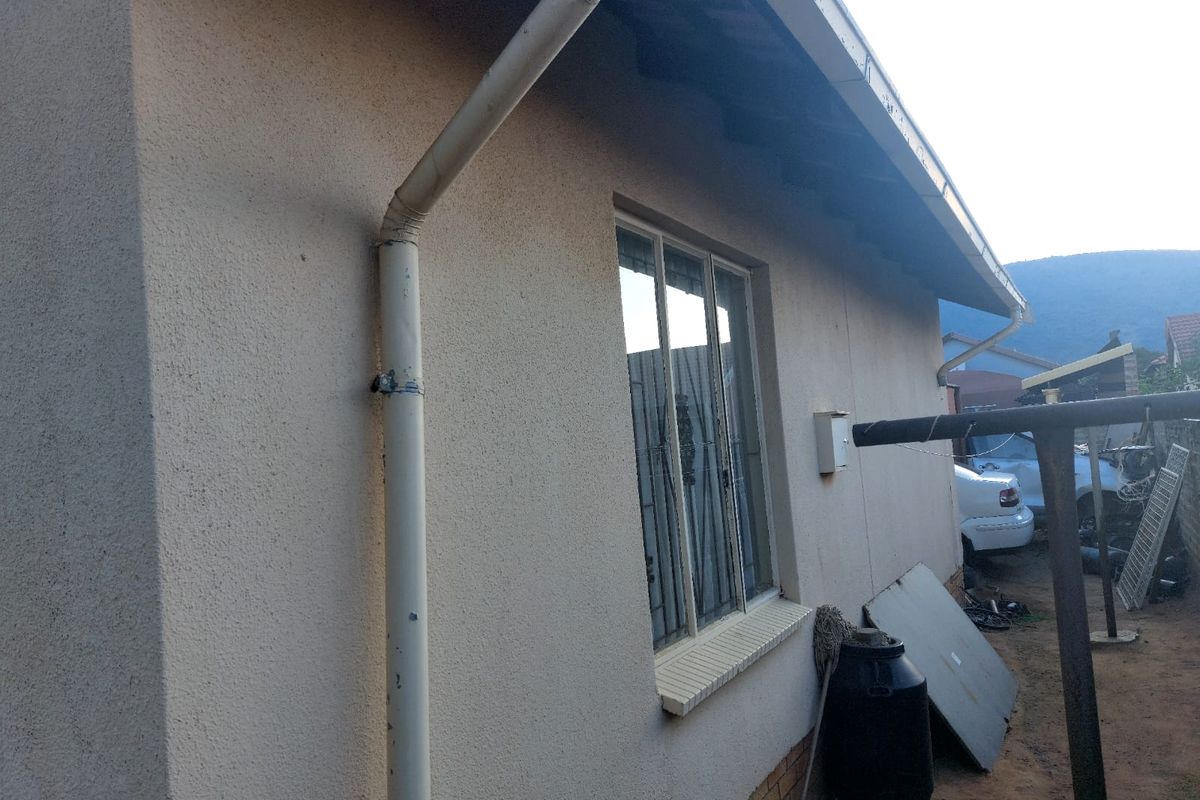 Rear exterior view of the house showing plastered walls, a window with security bars, and a downpipe system.