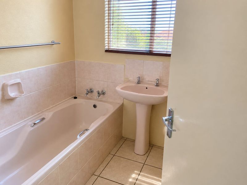 A functional bathroom featuring a pedestal basin, built-in bathtub with tiled surround, and ceramic floor tiles, offering a clean and neutral space.