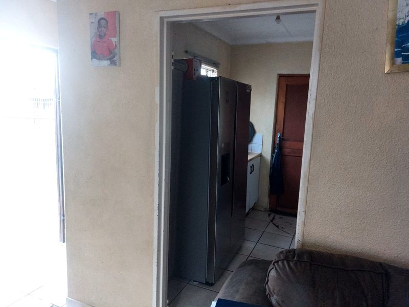 A view into a kitchen area featuring tiled flooring and wooden door access, showing signs of wear and requiring cosmetic updates.