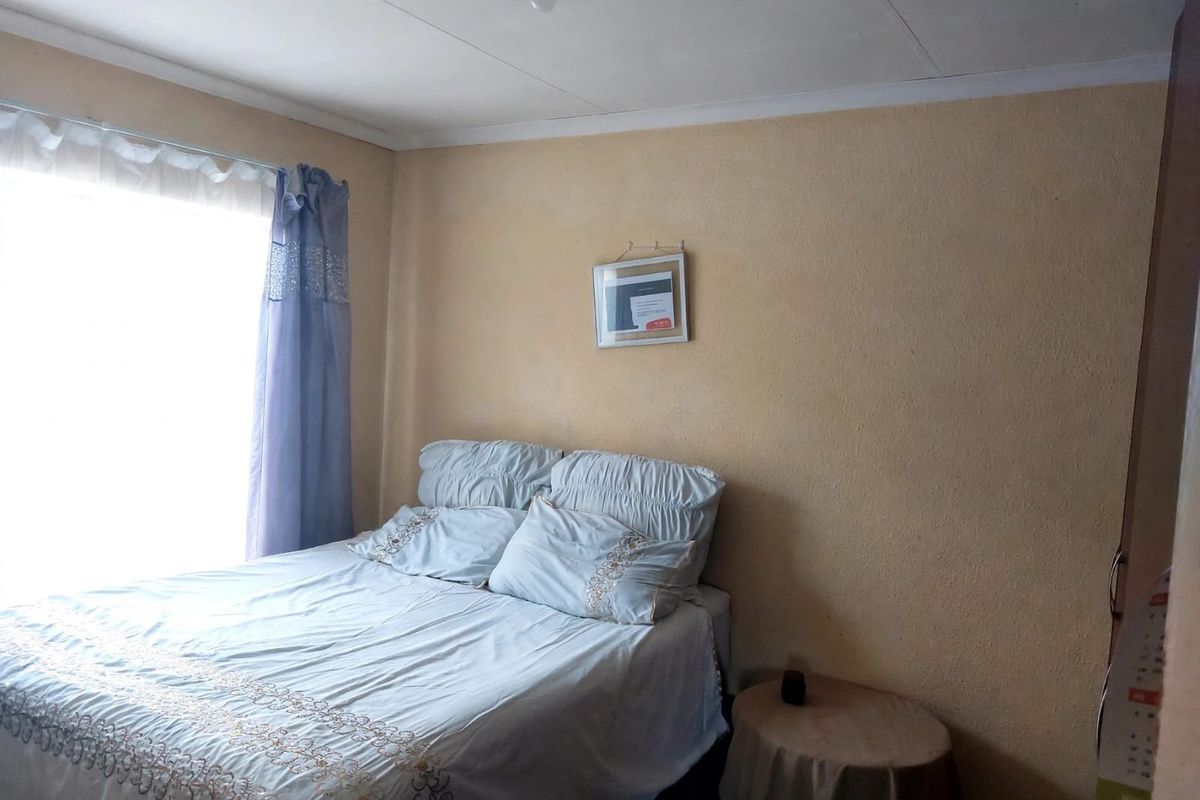 A compact bedroom featuring a window with natural light, textured walls, and a simple ceiling fixture.