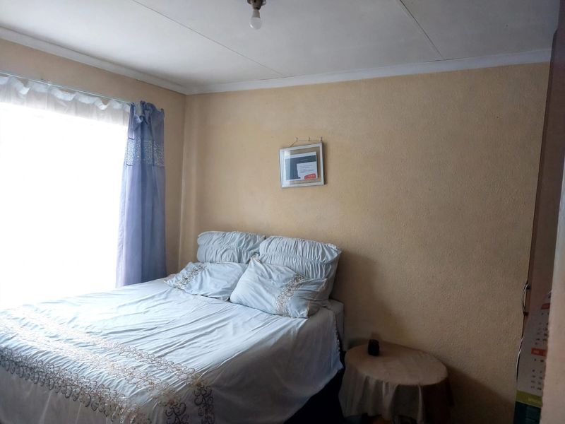 A compact bedroom featuring a window with natural light, textured walls, and a simple ceiling fixture.