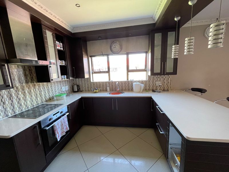 A well-appointed kitchen featuring dark wood cabinetry, stone countertops, a mosaic tile backsplash, and a functional breakfast bar with integrated appliances.