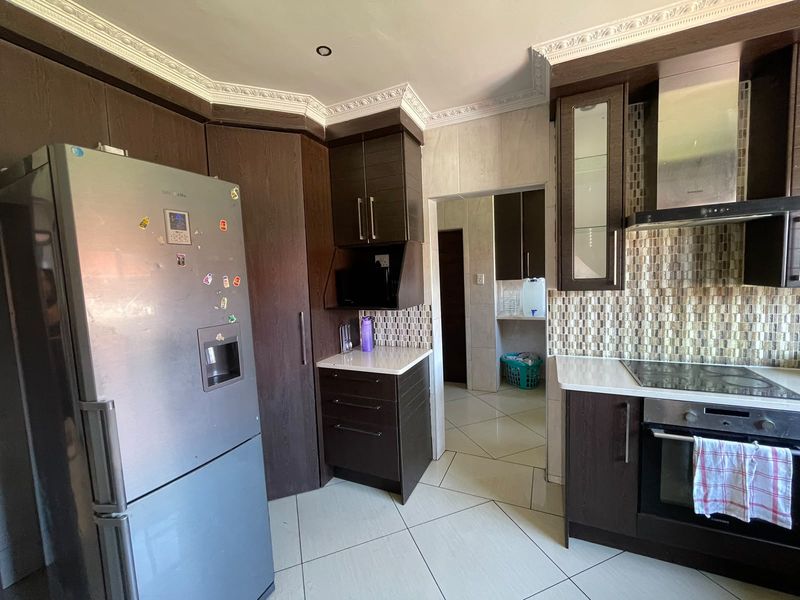 Modern kitchen featuring dark wood cabinetry, stone countertops, mosaic tile backsplash, and integrated appliances with tiled flooring and decorative crown molding.