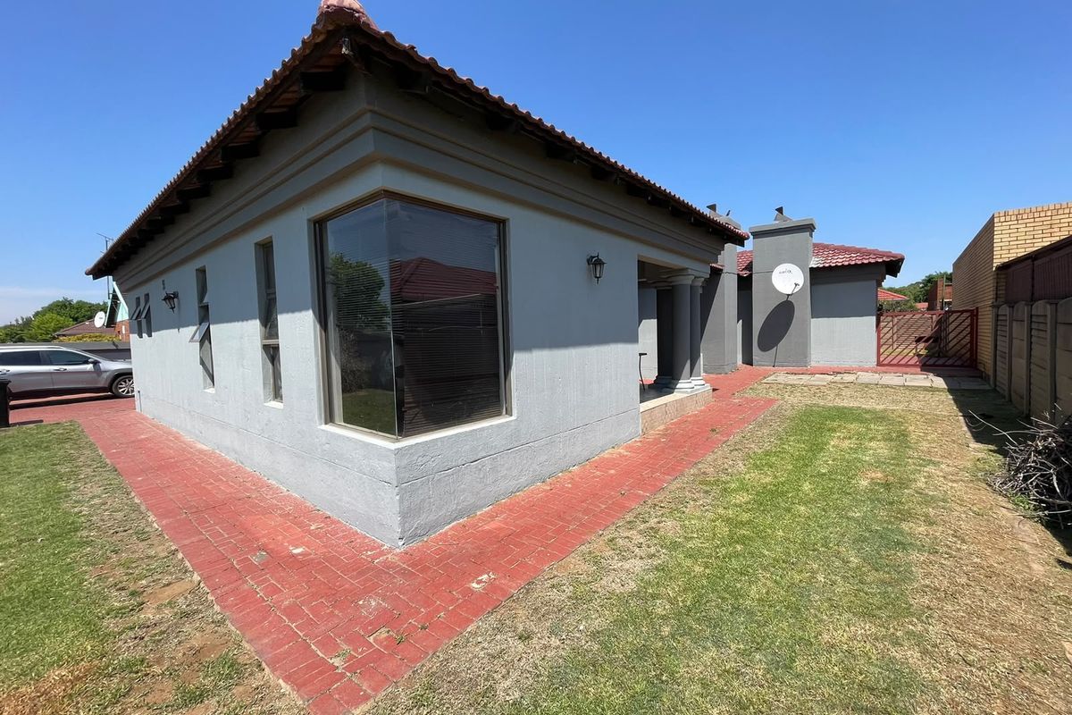 Rear exterior view of the house featuring a tiled roof, corner window, brick paved pathways, and a manageable garden area with boundary walling.