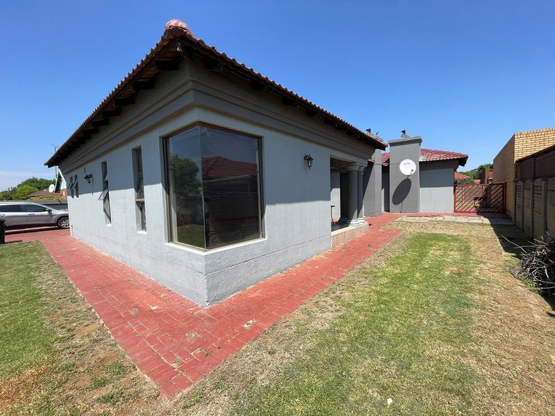Rear exterior view of the house featuring a tiled roof, corner window, brick paved pathways, and a manageable garden area with boundary walling.