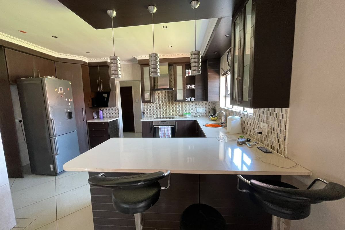 Modern kitchen featuring dark wood cabinetry, stone countertops, a breakfast bar, mosaic tile backsplash, and integrated appliances with contemporary pendant lighting.
