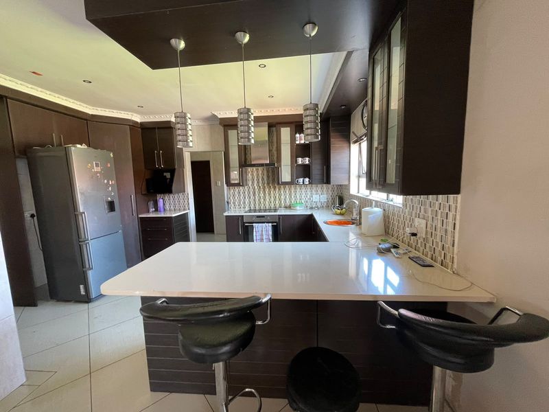Modern kitchen featuring dark wood cabinetry, stone countertops, a breakfast bar, mosaic tile backsplash, and integrated appliances with contemporary pendant lighting.
