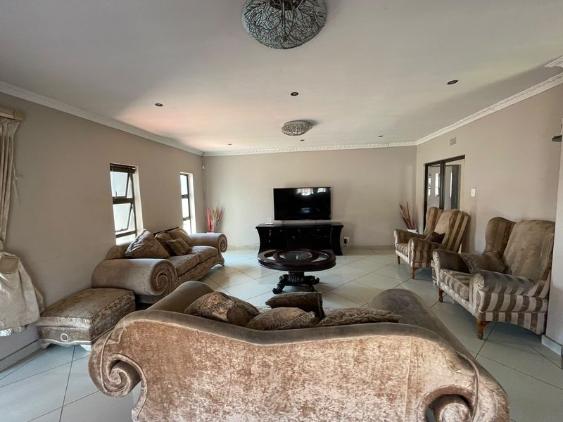 Spacious living room featuring neutral wall tones, tiled flooring, decorative ceiling cornices, and recessed lighting, providing a comfortable and well-lit area for relaxation.