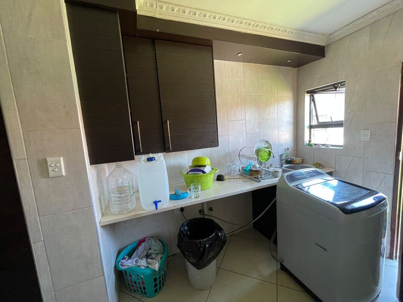 A functional laundry area featuring built-in dark wood cabinetry, tiled wall finishes, and a dedicated sink with plumbing connections for a washing machine.