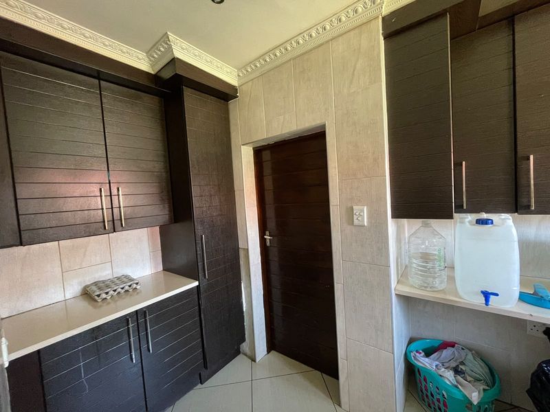 A functional scullery area featuring dark wood cabinetry, stone countertops, tiled splashbacks, and decorative ceiling cornicing.