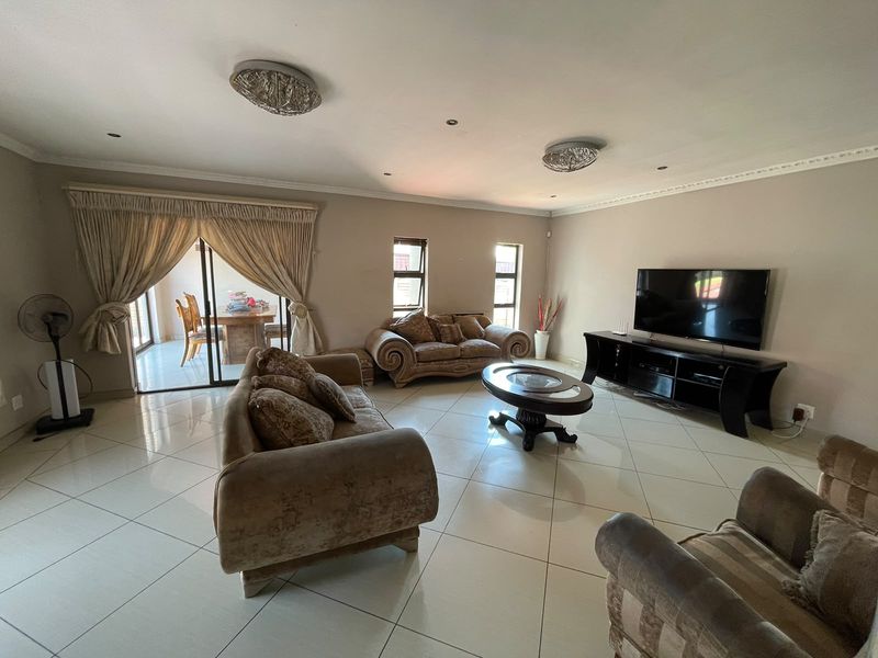 Spacious living room featuring large format floor tiles, recessed lighting, crown molding, and sliding glass doors leading to an outdoor patio area.