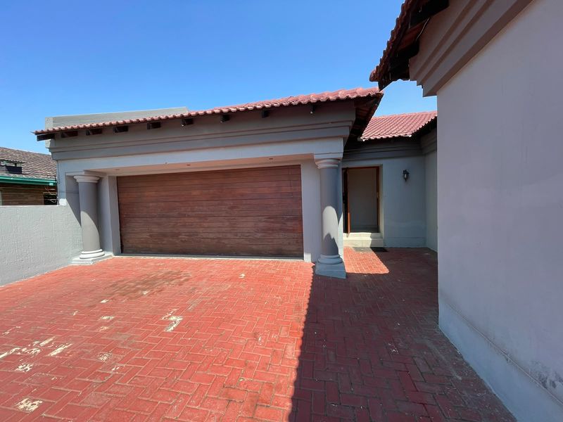 Front exterior view featuring a paved driveway, a wooden garage door, and a covered entrance area with decorative columns.