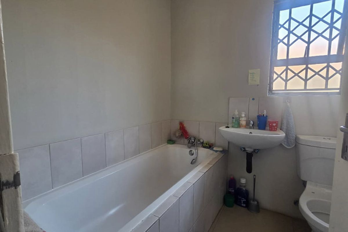 A functional bathroom featuring a bathtub, pedestal basin, and toilet, with security bars on the window and tiled splashback areas.
