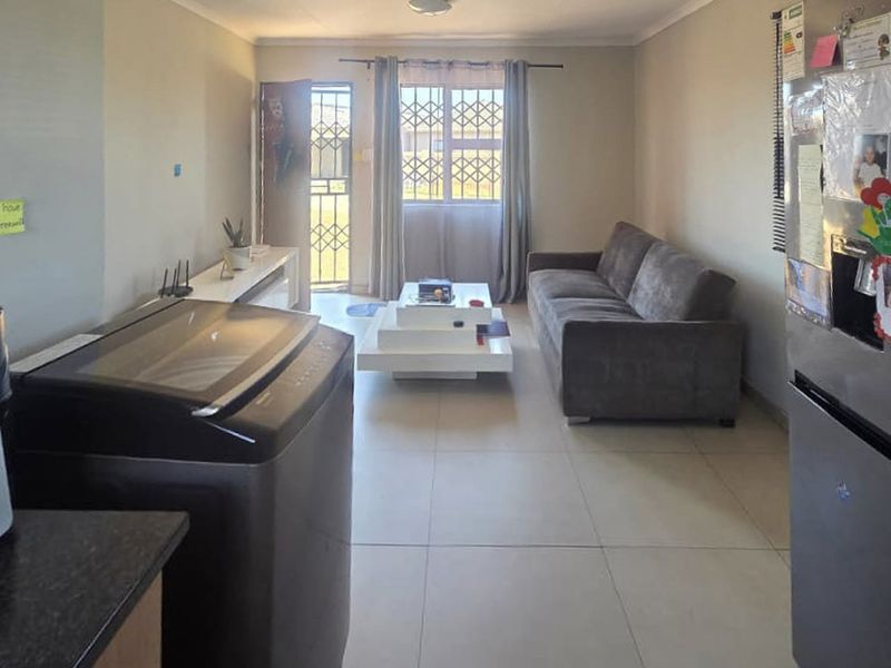 An open-plan living area featuring tiled flooring, a security gate, and a window with security bars, providing a functional and accessible layout.