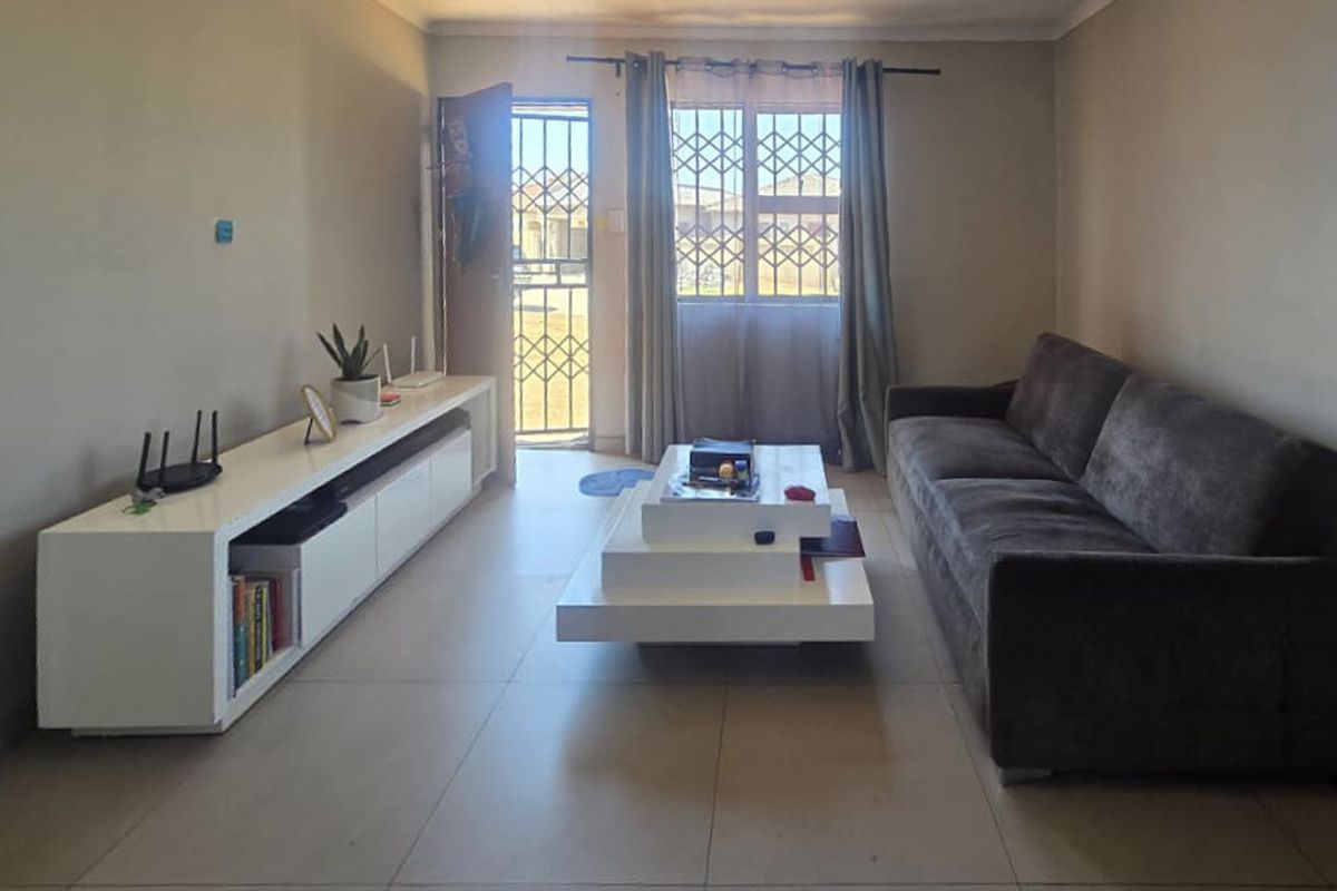 A functional living room featuring tiled flooring, a security gate at the entrance, and a window fitted with security bars.