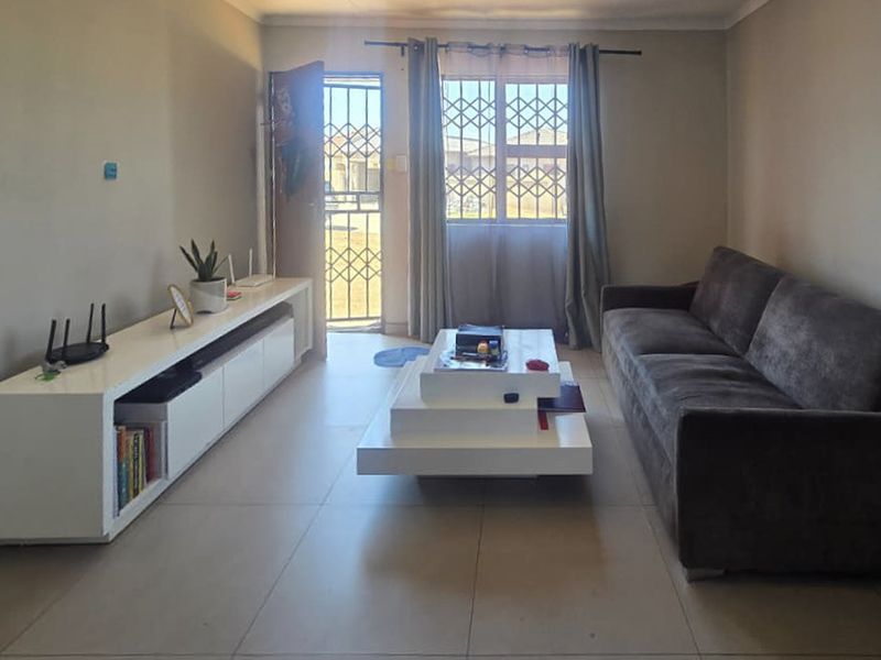 A functional living room featuring tiled flooring, a security gate at the entrance, and a window fitted with security bars.