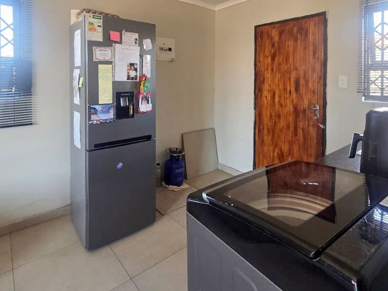 A functional laundry area featuring tiled flooring, security bars on the windows, and a wooden door.