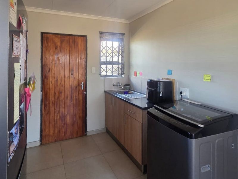 A functional laundry area featuring built-in cabinetry, a stainless steel sink, and tiled flooring, with a secure window and direct exterior access.
