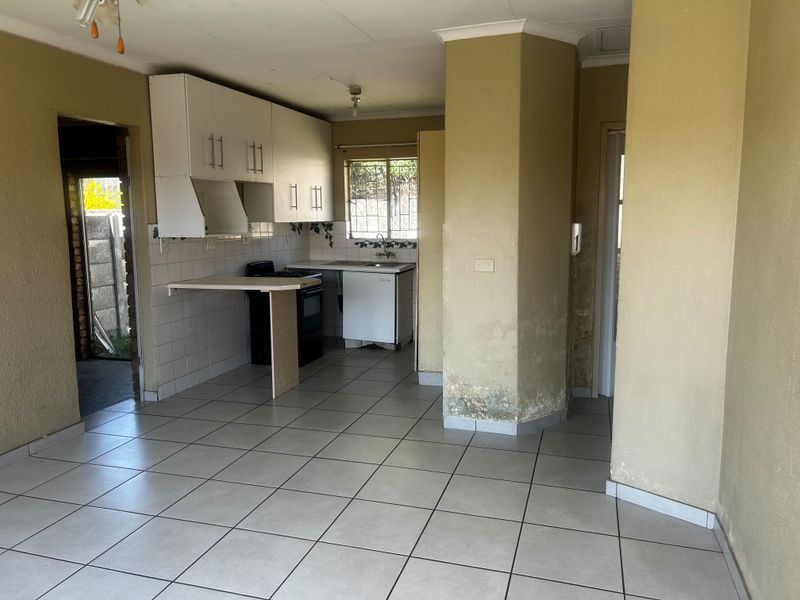 A functional kitchen area featuring tiled flooring, built-in cabinetry, and a stove, currently requiring maintenance and cosmetic updates to address wall damage.