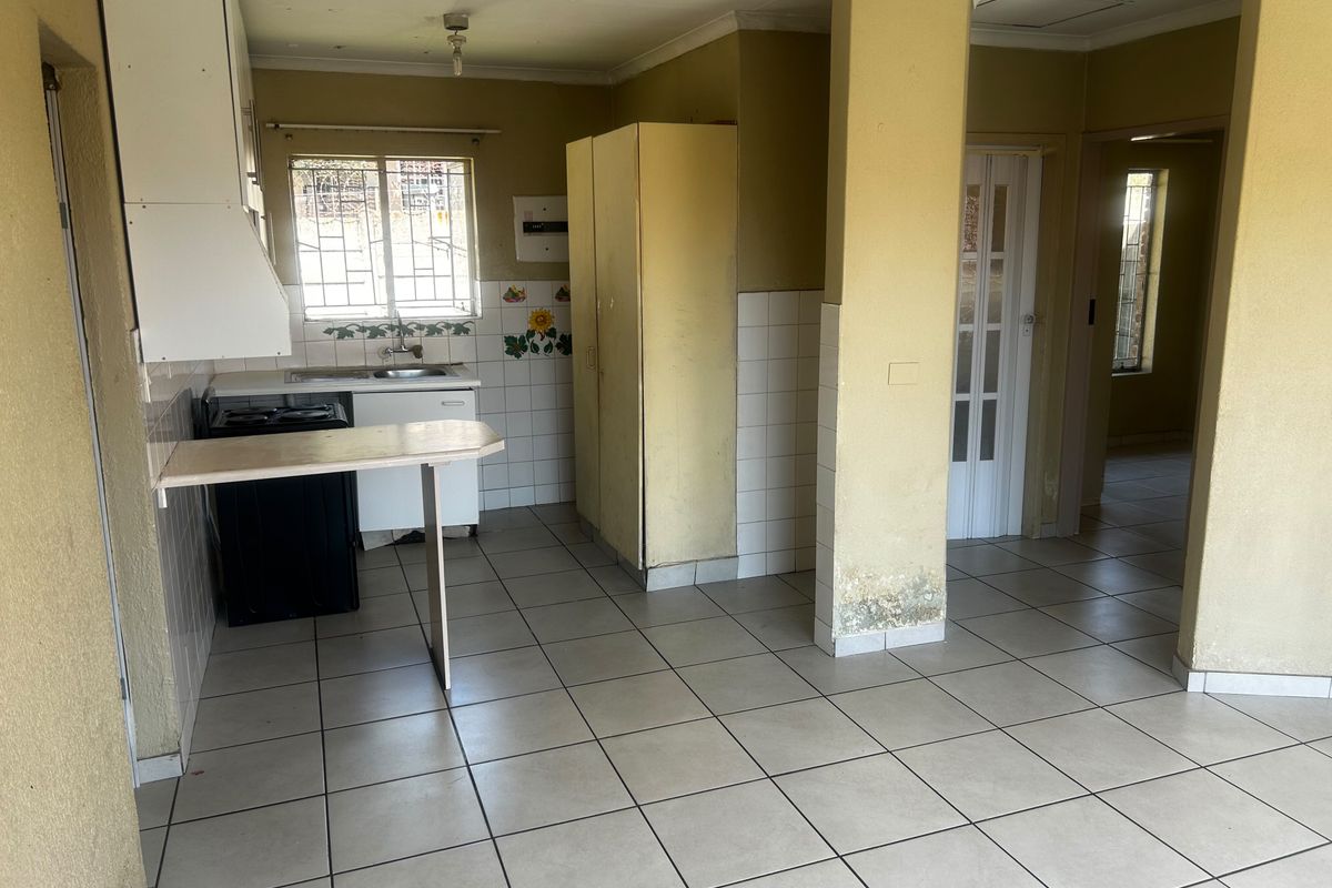 A dated kitchen area featuring tiled flooring, built-in cabinetry, and a sink, requiring cosmetic updates and repairs to address visible wall damage.