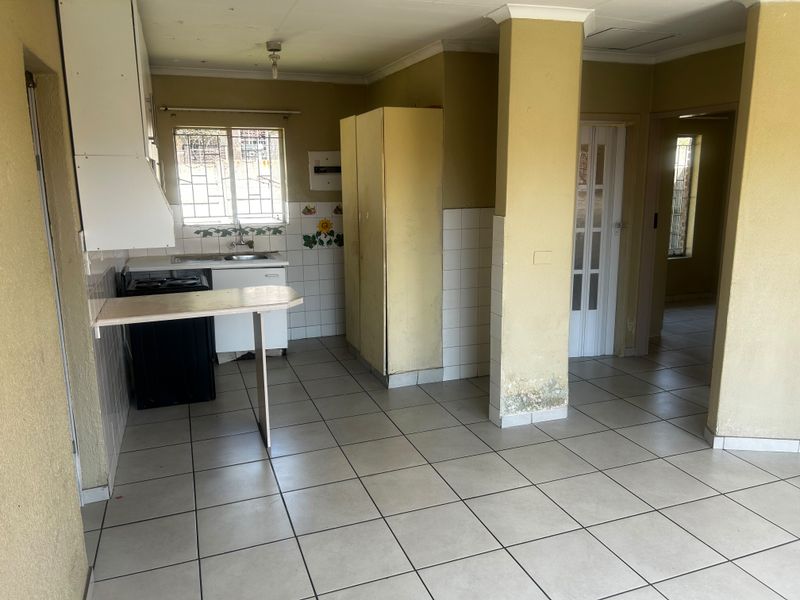 A dated kitchen area featuring tiled flooring, built-in cabinetry, and a sink, requiring cosmetic updates and repairs to address visible wall damage.