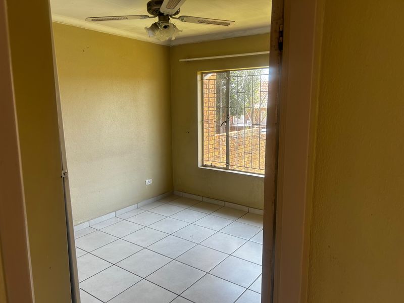 An empty bedroom featuring tiled flooring, a ceiling fan, and security bars on the window, awaiting personal touches to enhance the space.