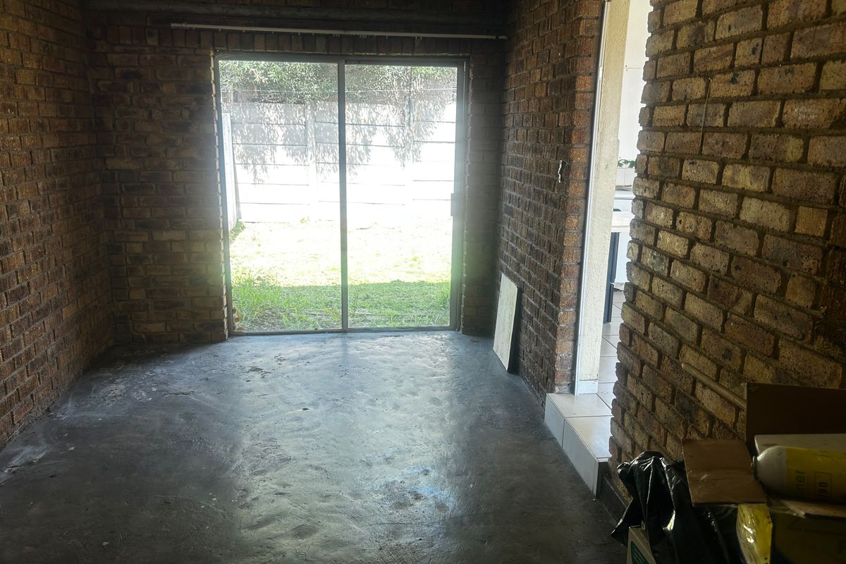 An empty living area featuring exposed brick walls, concrete flooring, and a sliding glass door providing access to the rear garden.