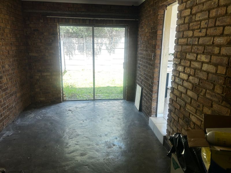 An empty living area featuring exposed brick walls, concrete flooring, and a sliding glass door providing access to the rear garden.