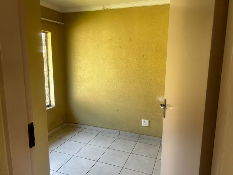 An empty bedroom featuring tiled flooring and a vertical window, requiring cosmetic updates to the wall finishes and ceiling.