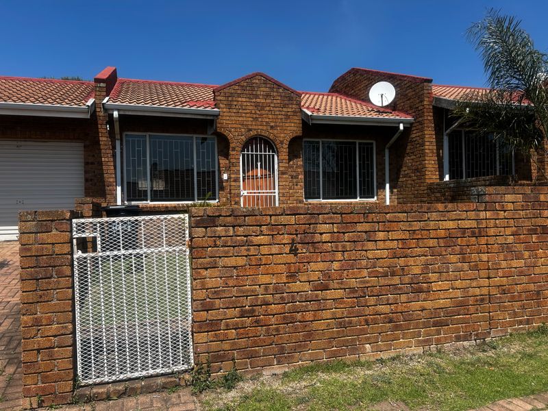 Front elevation of a face brick townhouse featuring a tiled roof, secure gated entrance, and integrated garage.