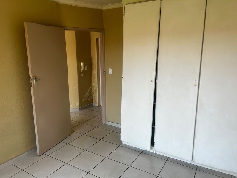 An empty bedroom featuring tiled flooring and built-in cupboards, showing signs of wall surface damage and peeling paint requiring maintenance.
