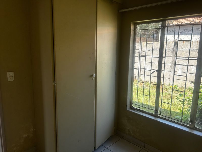 An empty bedroom featuring built-in wardrobes, tiled flooring, and security bars on the window, requiring cosmetic updates to the walls.