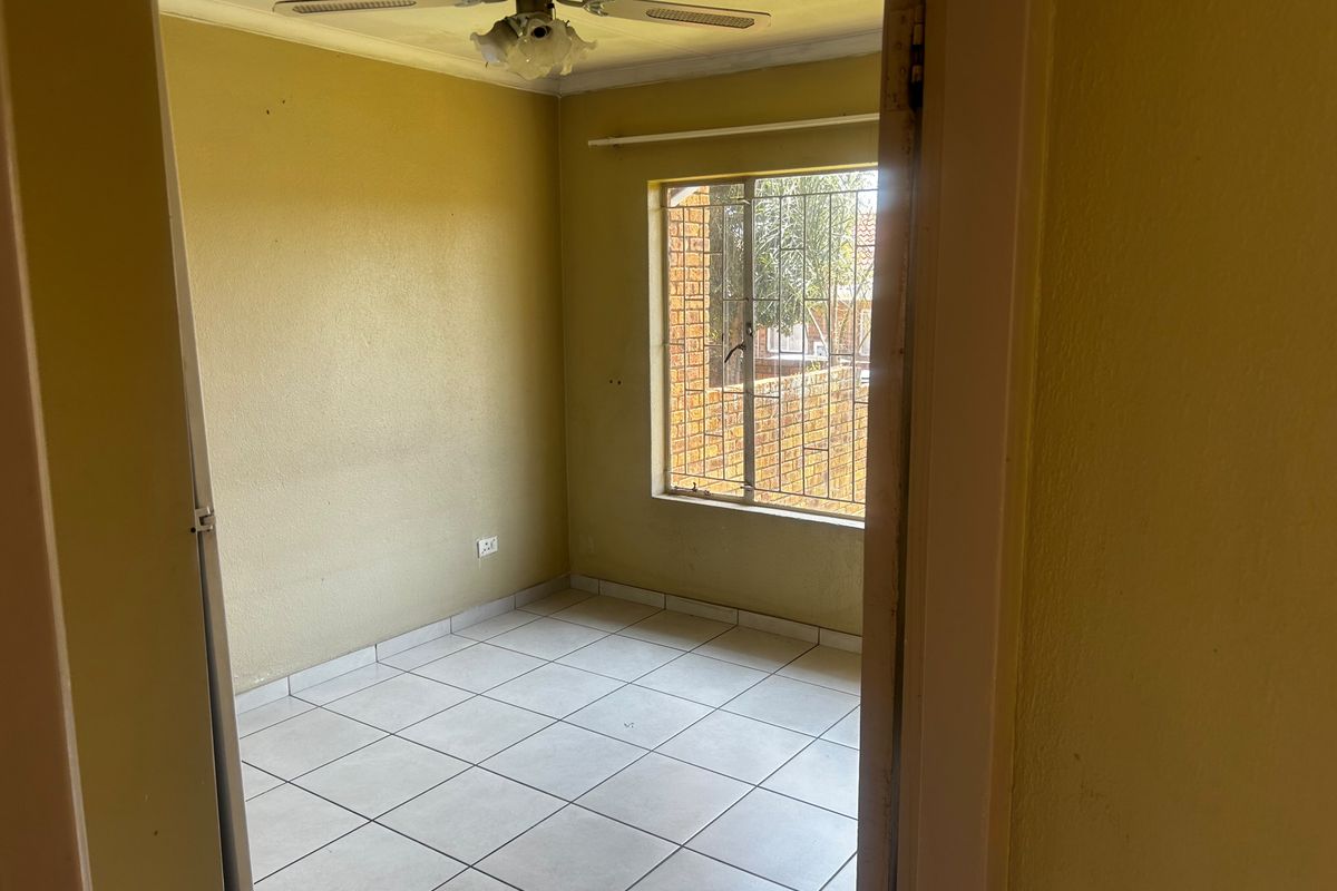An empty bedroom featuring tiled flooring, a ceiling fan, and security bars on the window, offering a blank canvas for potential updates.