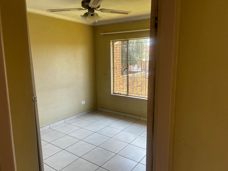 An empty bedroom featuring tiled flooring, a ceiling fan, and security bars on the window, offering a blank canvas for potential updates.
