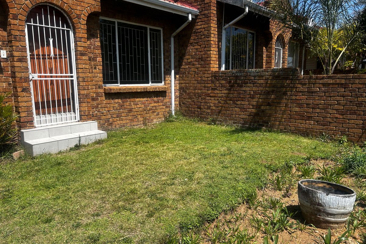 A rear exterior view of a face brick townhouse featuring a small private garden, security gate, and tiled entrance steps.