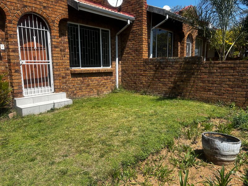 A rear exterior view of a face brick townhouse featuring a small private garden, security gate, and tiled entrance steps.