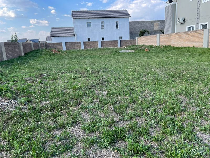 A vacant residential plot featuring a grass lawn enclosed by perimeter brick boundary walls in a developed estate setting.