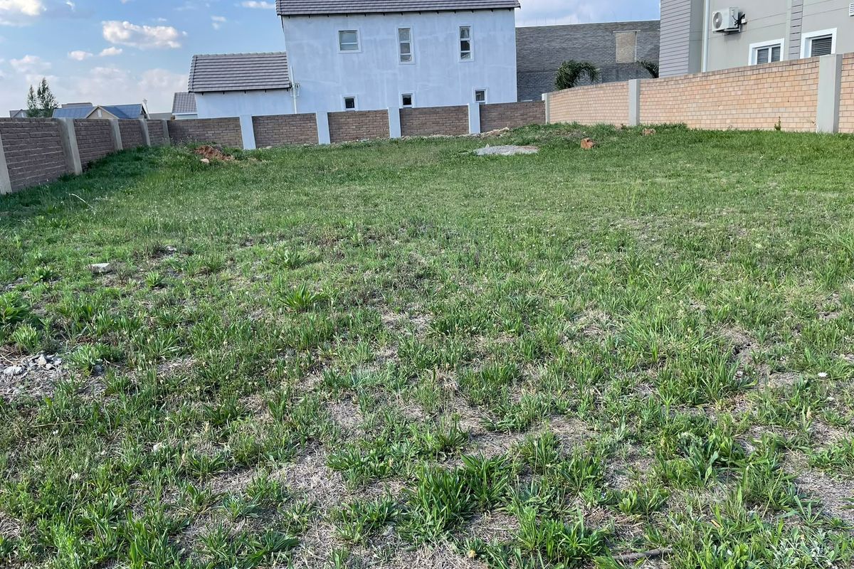 A vacant residential plot featuring a grass lawn enclosed by perimeter brick boundary walls.