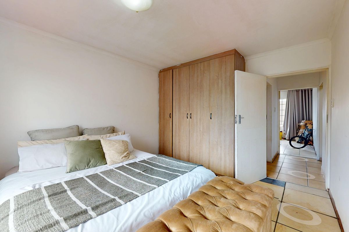 A bedroom featuring built-in wooden wardrobes and tiled flooring, with an adjacent hallway visible through the doorway.