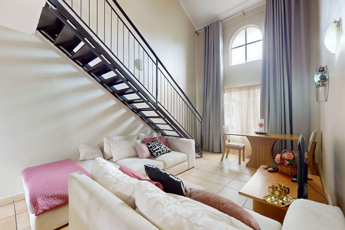 Spacious living area featuring a striking metal staircase, high vaulted ceilings, and a large arched window that allows for abundant natural light.